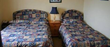 A room with two beds, each with a patterned bedspread, a bedside table with a lamp, and a framed picture on the wall.
