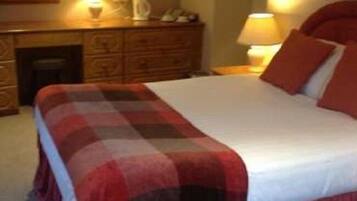 Un lit bien fait, recouvert d’une couverture à carreaux, une commode en bois avec une lampe, et une table de chevet avec une lampe.