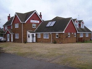 Een gebouw met twee verdiepingen, een gevel in rood en bruin, een bord waarop 'Boston Lodge' staat en een kleine garage ernaast.