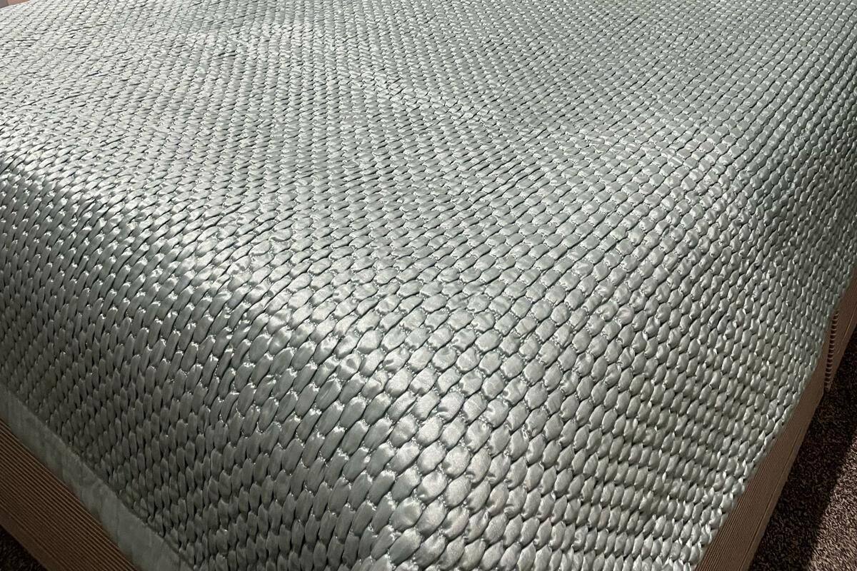 A neatly made bed with a textured blanket, a patterned wall, and a lamp on a bedside table.
