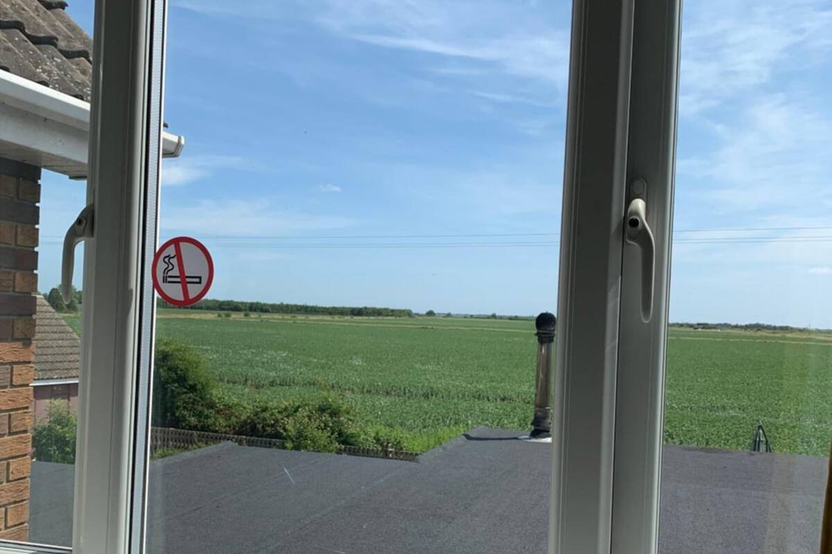 A window with a no-smoking sign, a view of a green field, and a clear blue sky.