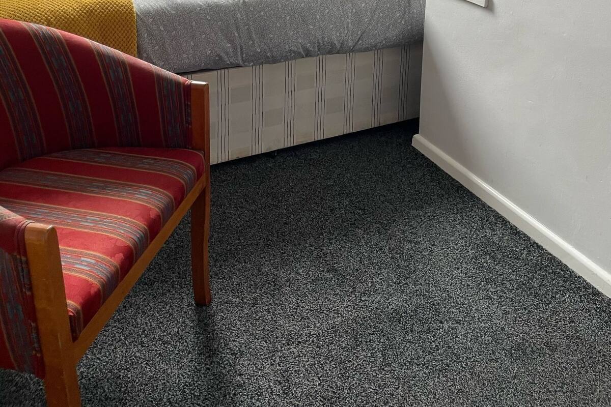 A compact room with a built-in bed, a red striped chair, and a window with curtains.