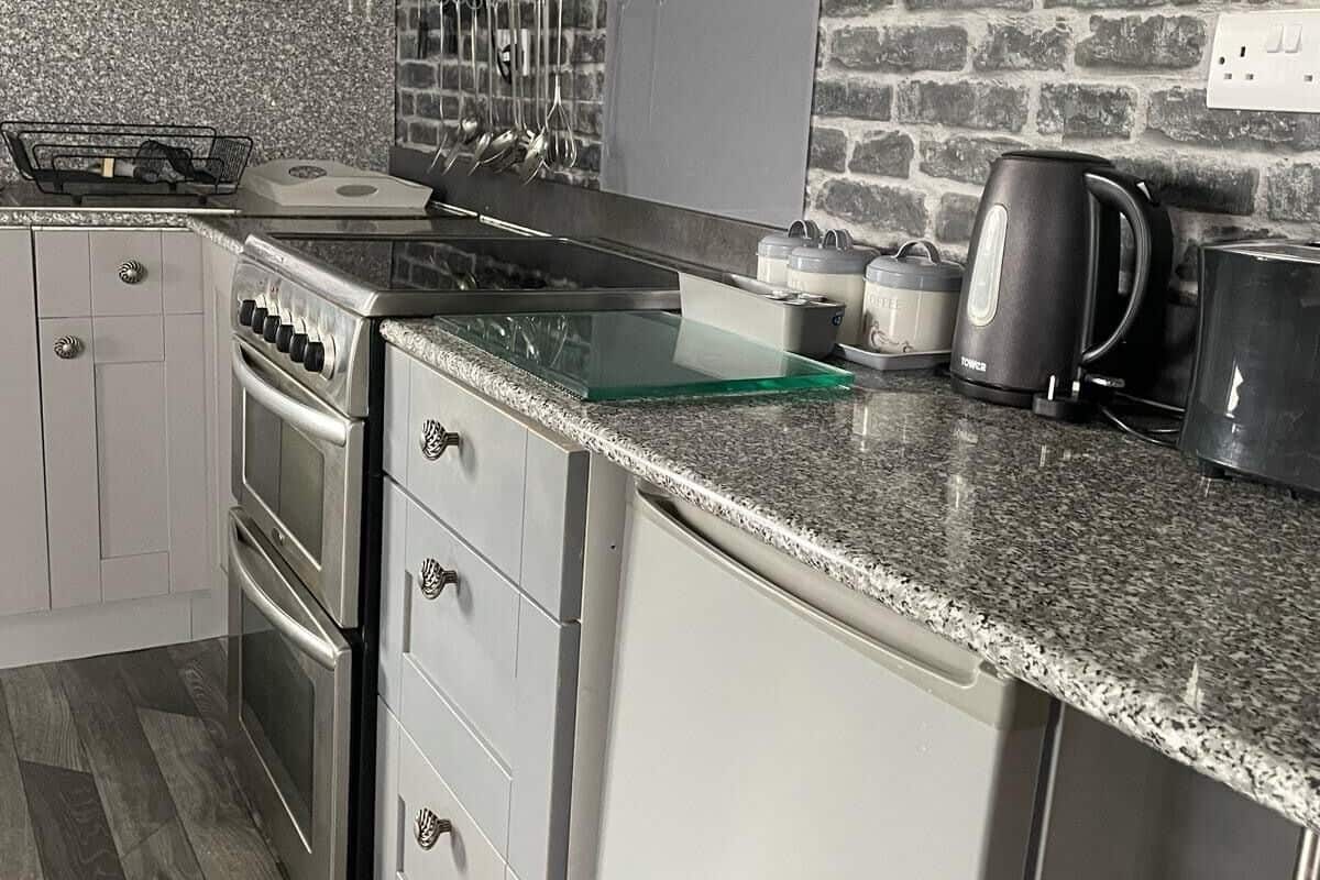 A modern kitchen with a granite countertop, stainless steel appliances, and a brick wall backsplash.