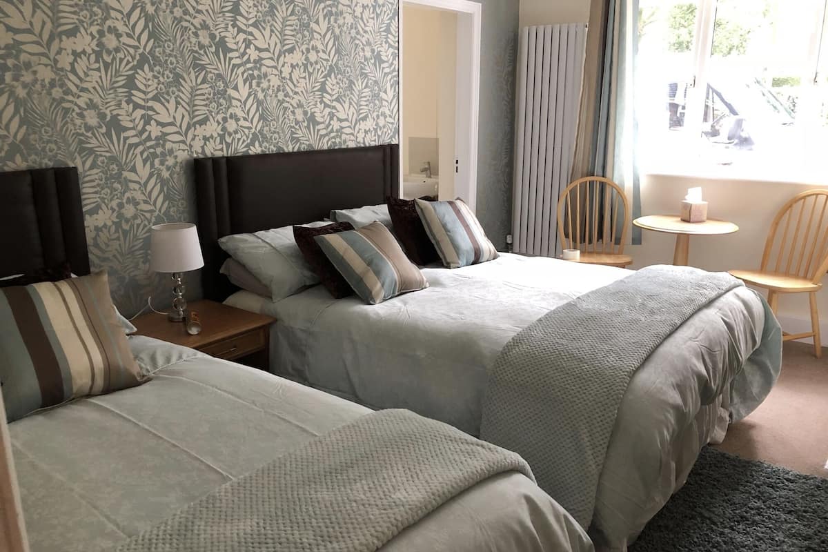 A hotel room with two beds, a nightstand, a lamp, a chair, and a window with a view of the outside.