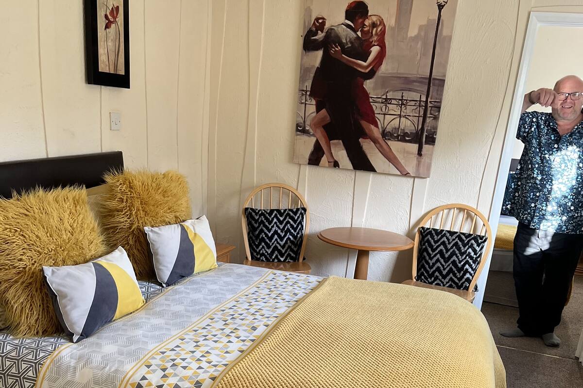 A bedroom with a bed, two chairs, a table, and artwork on the walls.