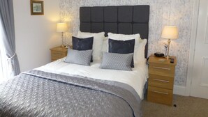 A neatly made bed with a grey quilt, two bedside tables with lamps, and a floral wallpaper pattern. - Bryn Derwen Guest House (Conwy)