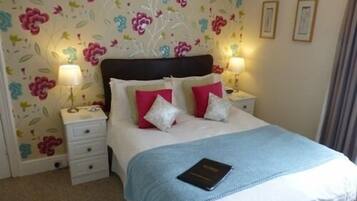 A neatly made bed with a blue blanket and pillows, two bedside lamps, and a floral wallpaper pattern.