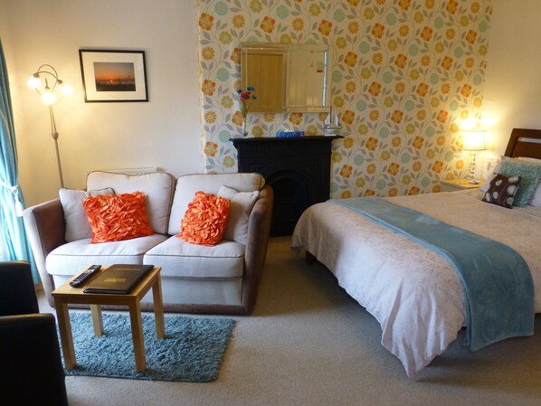 A cozy room with a sofa, a small table, a bed, and a fireplace. - Bryn Derwen Guest House (Conwy)