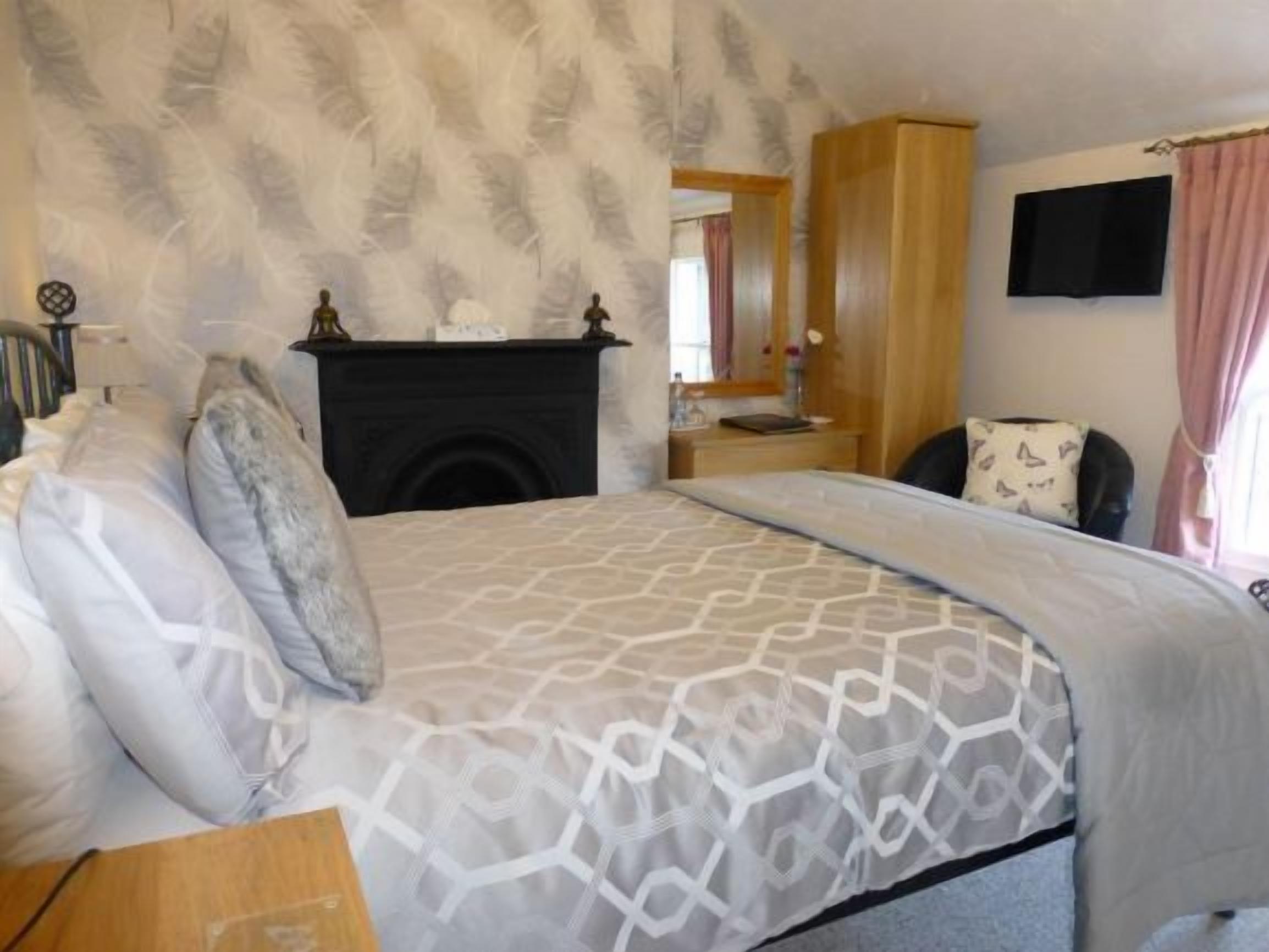 Un dormitorio con una colcha estampada, chimenea, armario de madera, televisor y espejo.