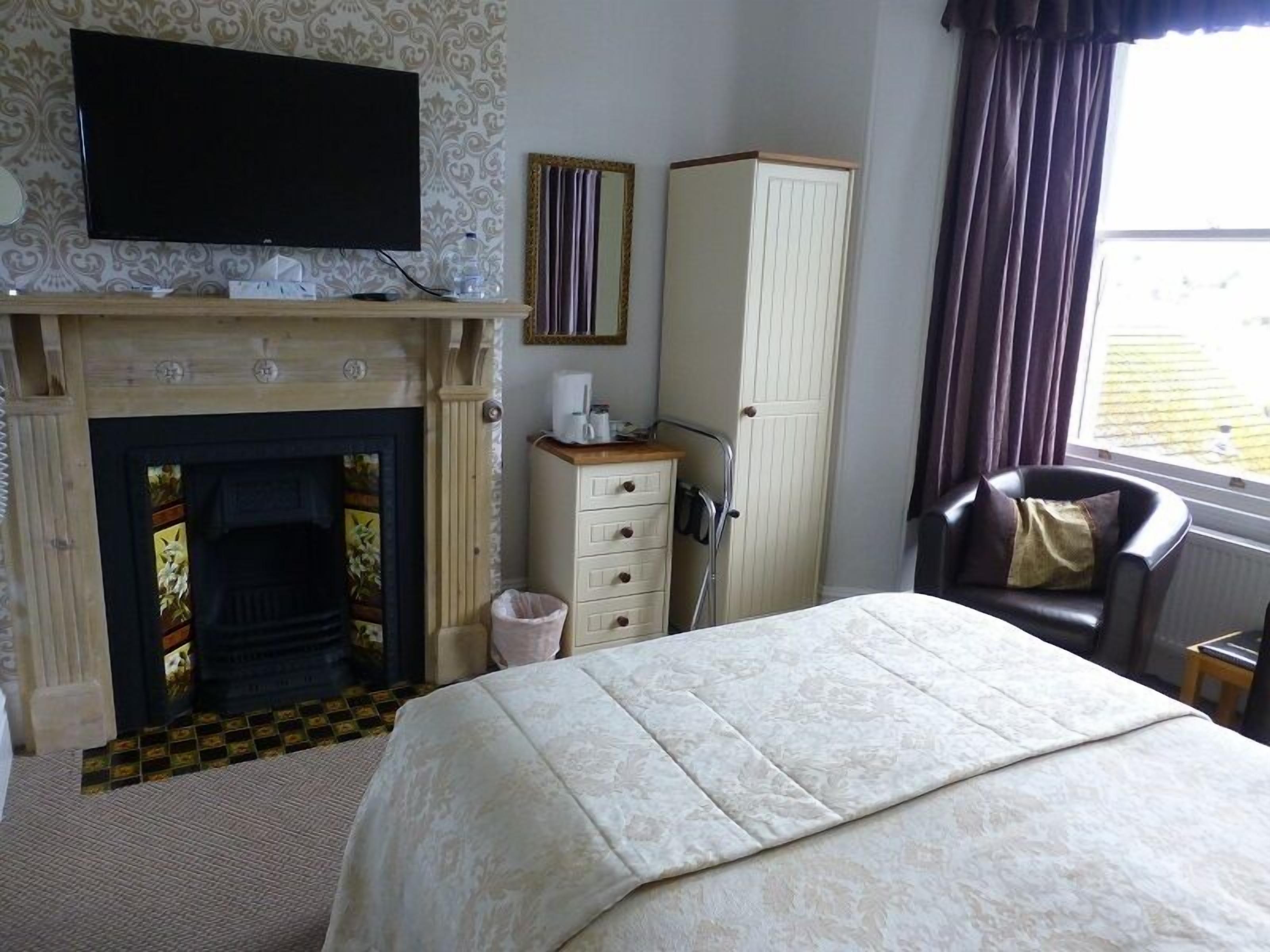 A hotel room with a fireplace, a television, a wardrobe, a chair, and a bed.