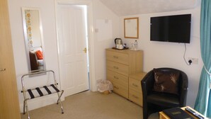 A room with a bed, a chair, a TV, a dresser, and a small table with a remote control. - Bryn Derwen Guest House (Conwy)