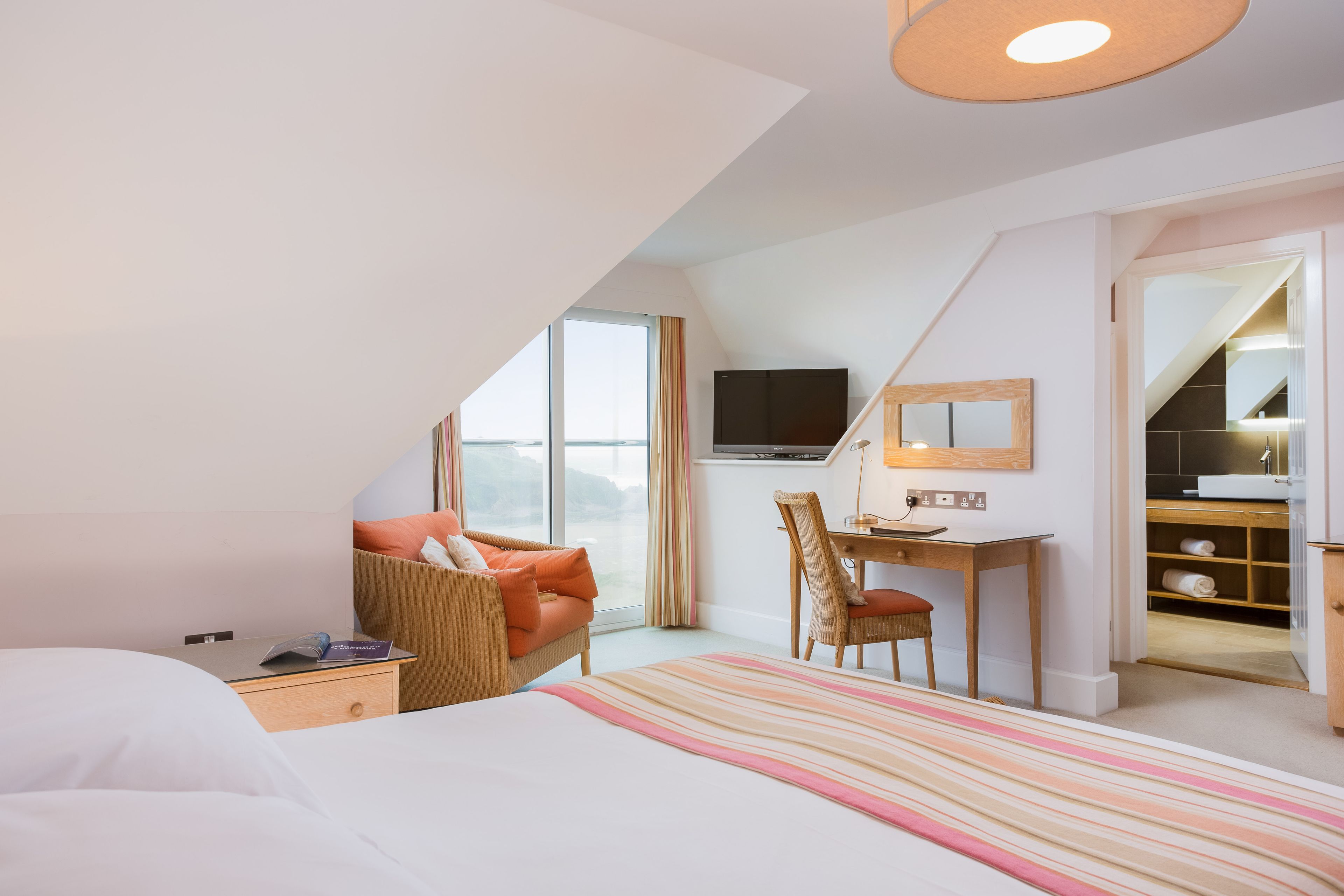 Habitación de hotel moderna con cama, escritorio, silla, televisor y vistas al exterior.