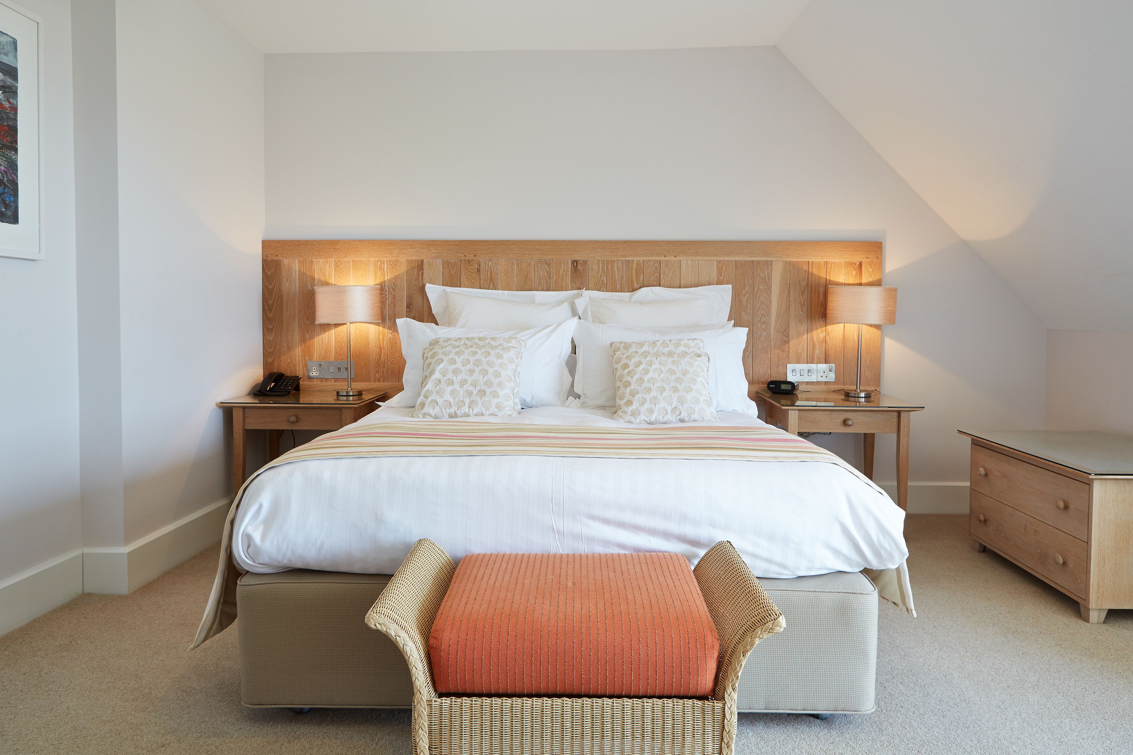A neatly arranged bedroom with a large bed, two bedside tables, a nightstand, a chair, and a small wooden dresser.