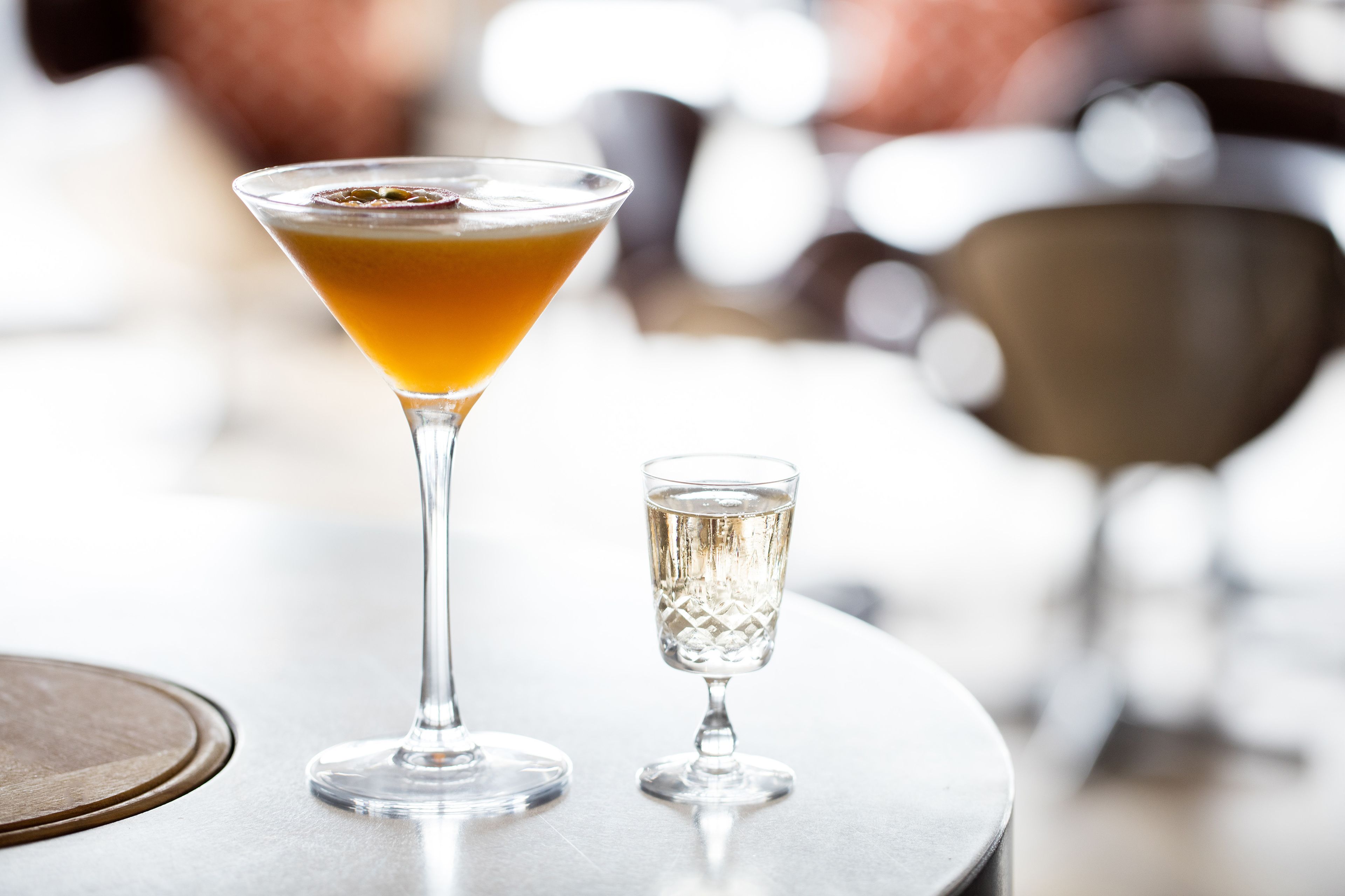 Una copa de martini y una copa pequeña sobre una mesa redonda.