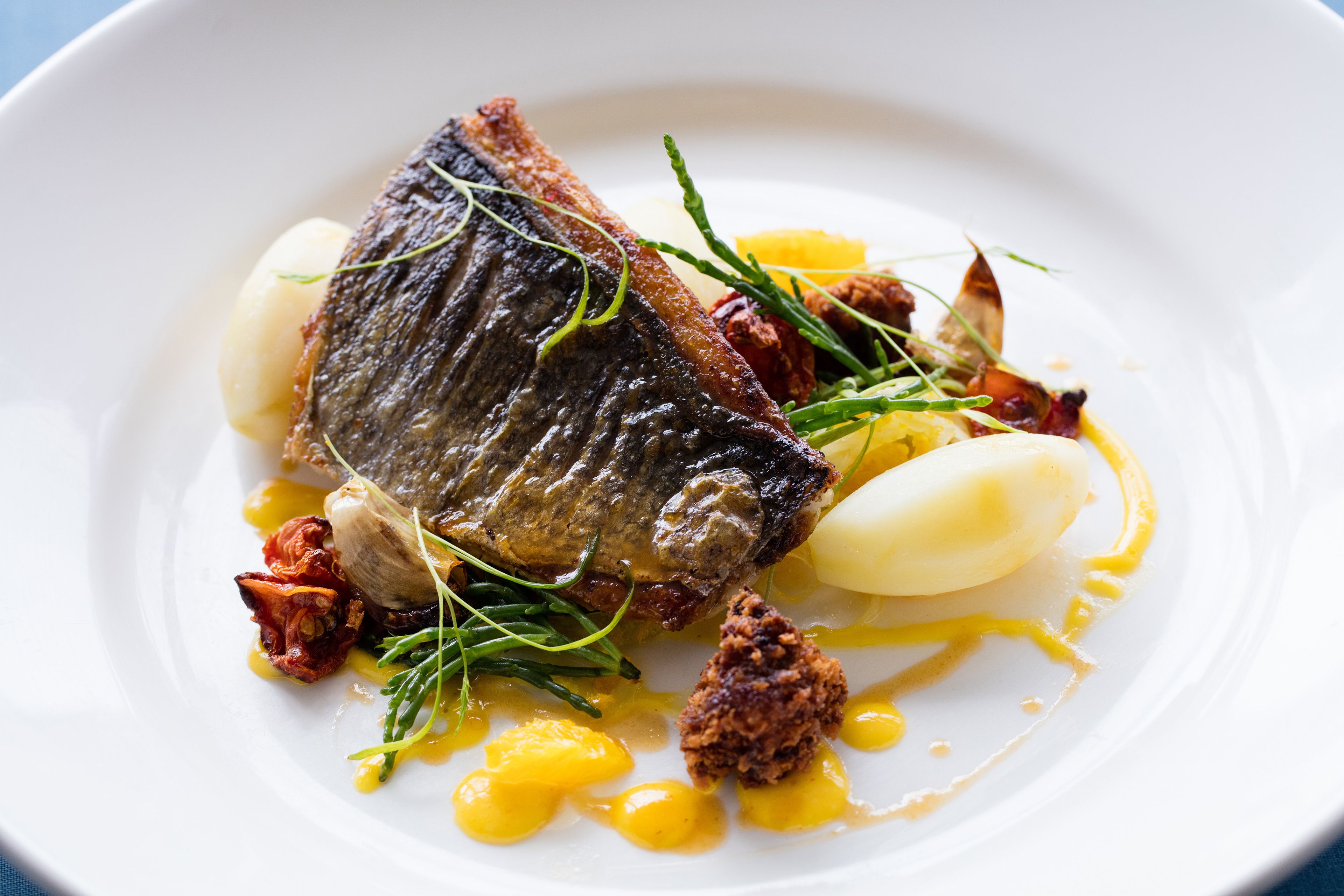 Un plato con pescado, patatas y guarniciones.