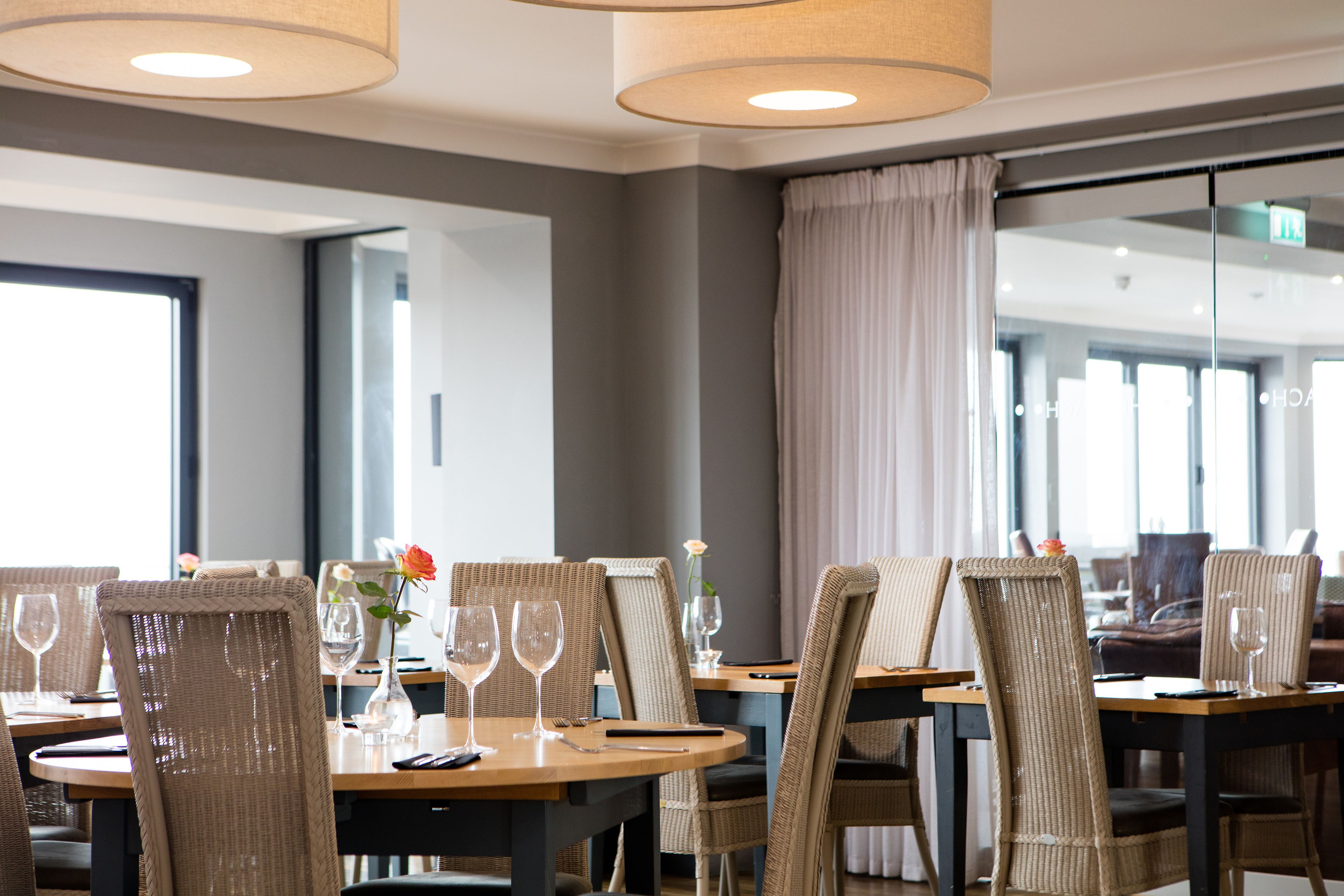 A dining area with round tables, wicker chairs, and glassware.
