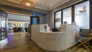 A reception area with a curved counter labeled "THE BEACH" and a seating area with a director's chair.