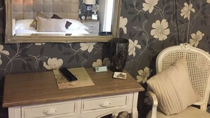 A bedroom with a large mirror, a bed with white bedding, a small bedside table with a lamp, and a chair with a cushion. - Castle Lodge Hotel (Ross-on-Wye)