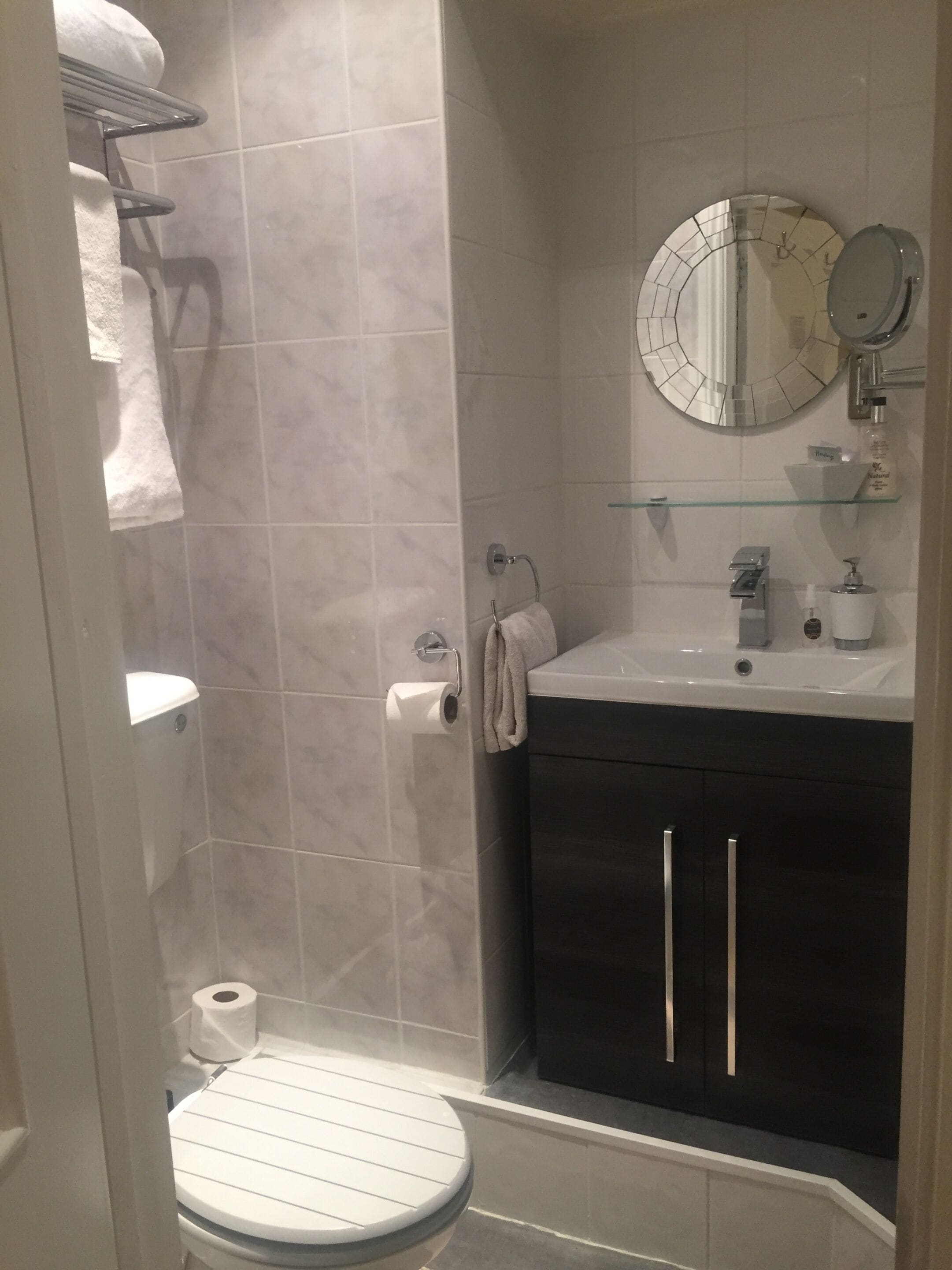 Un baño con inodoro, ducha, lavamanos con espejo y toallero.