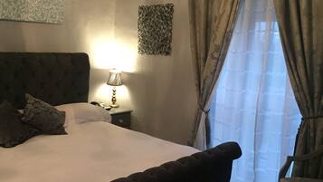 Un dormitorio con una cama grande, una lámpara de noche, una silla y una ventana con cortinas.