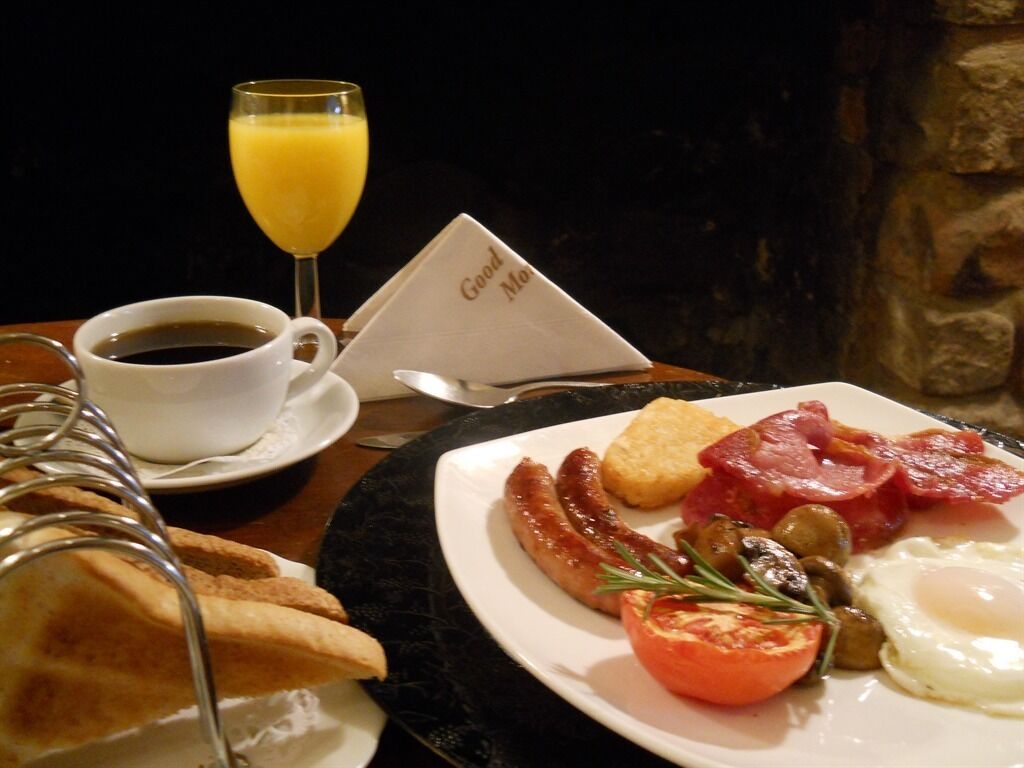 A breakfast plate with eggs, bacon, sausage, toast, and a glass of orange juice.