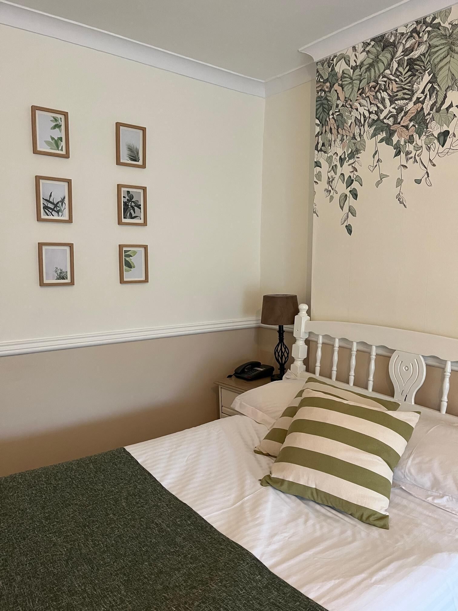 Una camera d'albergo con un letto, un comodino, una lampada e una parete decorata con stampe di piante.
