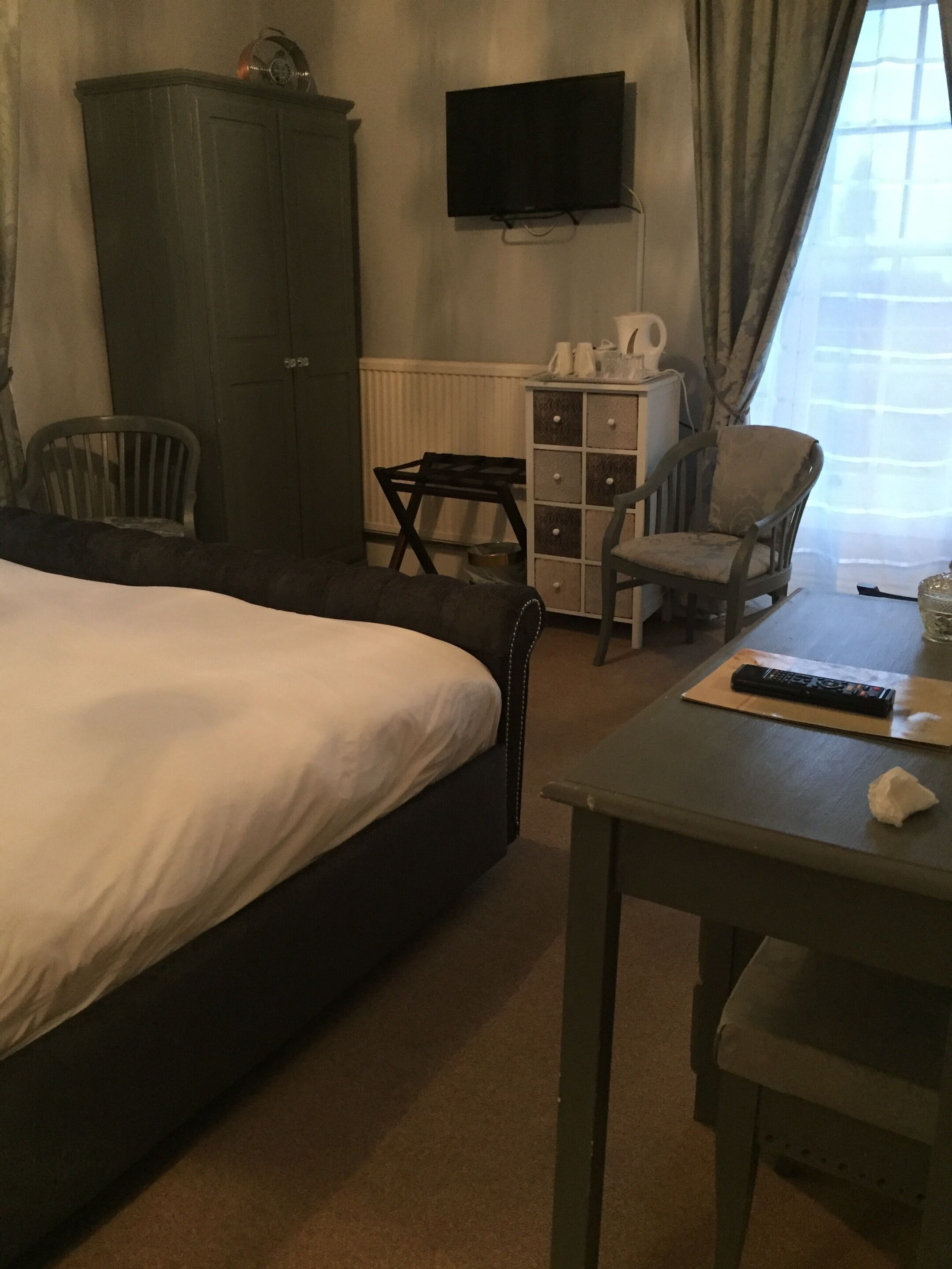 A hotel room with a bed, a TV, a wardrobe, a small table with a remote control, and a chair.