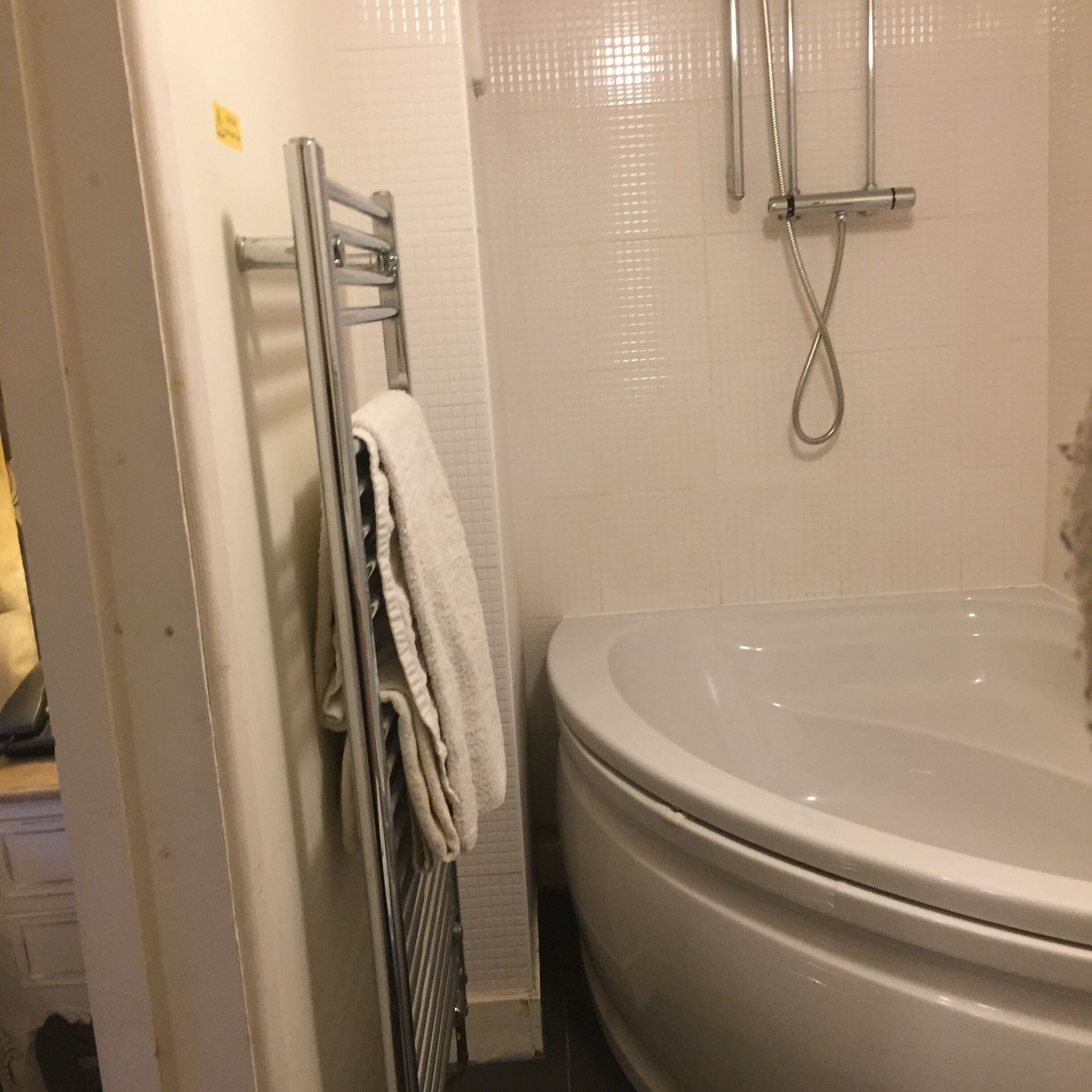 Un baño con bañera, un perchero con toallas y un cabezal de ducha.