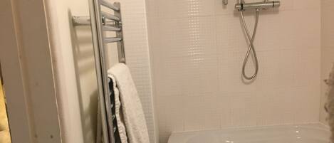 A bathroom with a bathtub, a towel rack with towels, and a shower head.