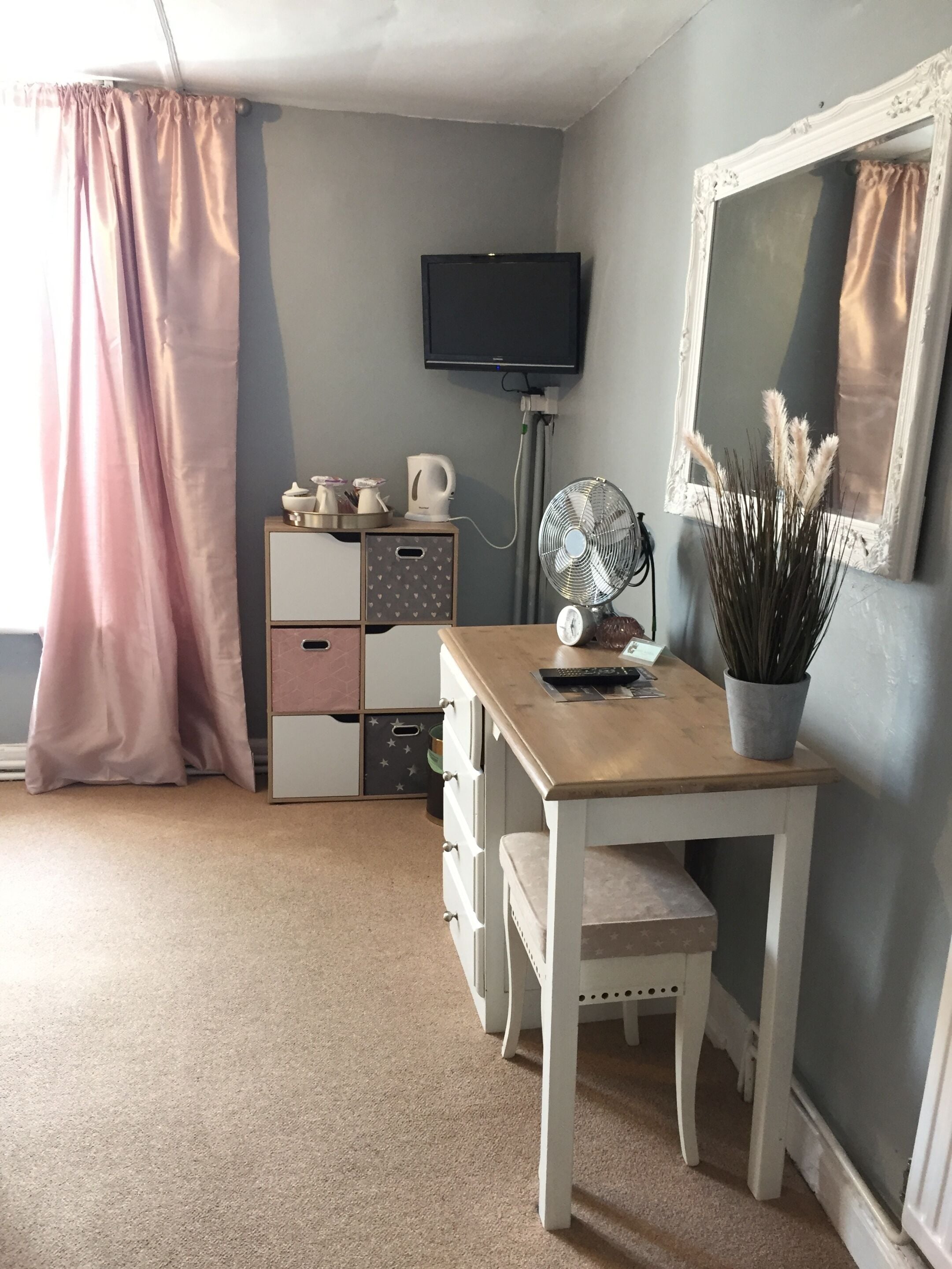 Ein Zimmer mit einem Holztisch, einem Fernseher, einem Ventilator, einem Schminktisch und einer Topfpflanze.