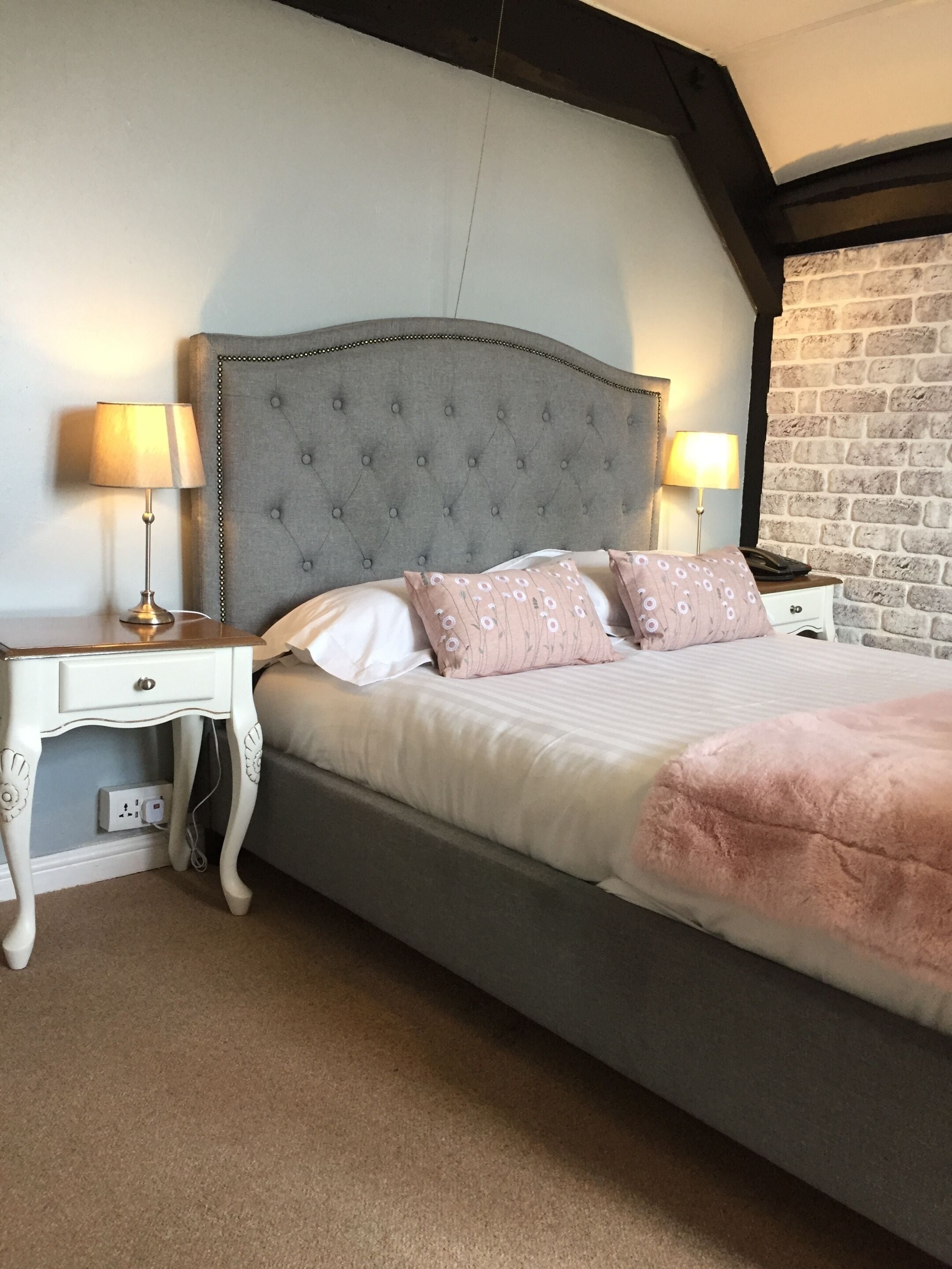 A bedroom with a large bed, two bedside tables, and a brick wall.