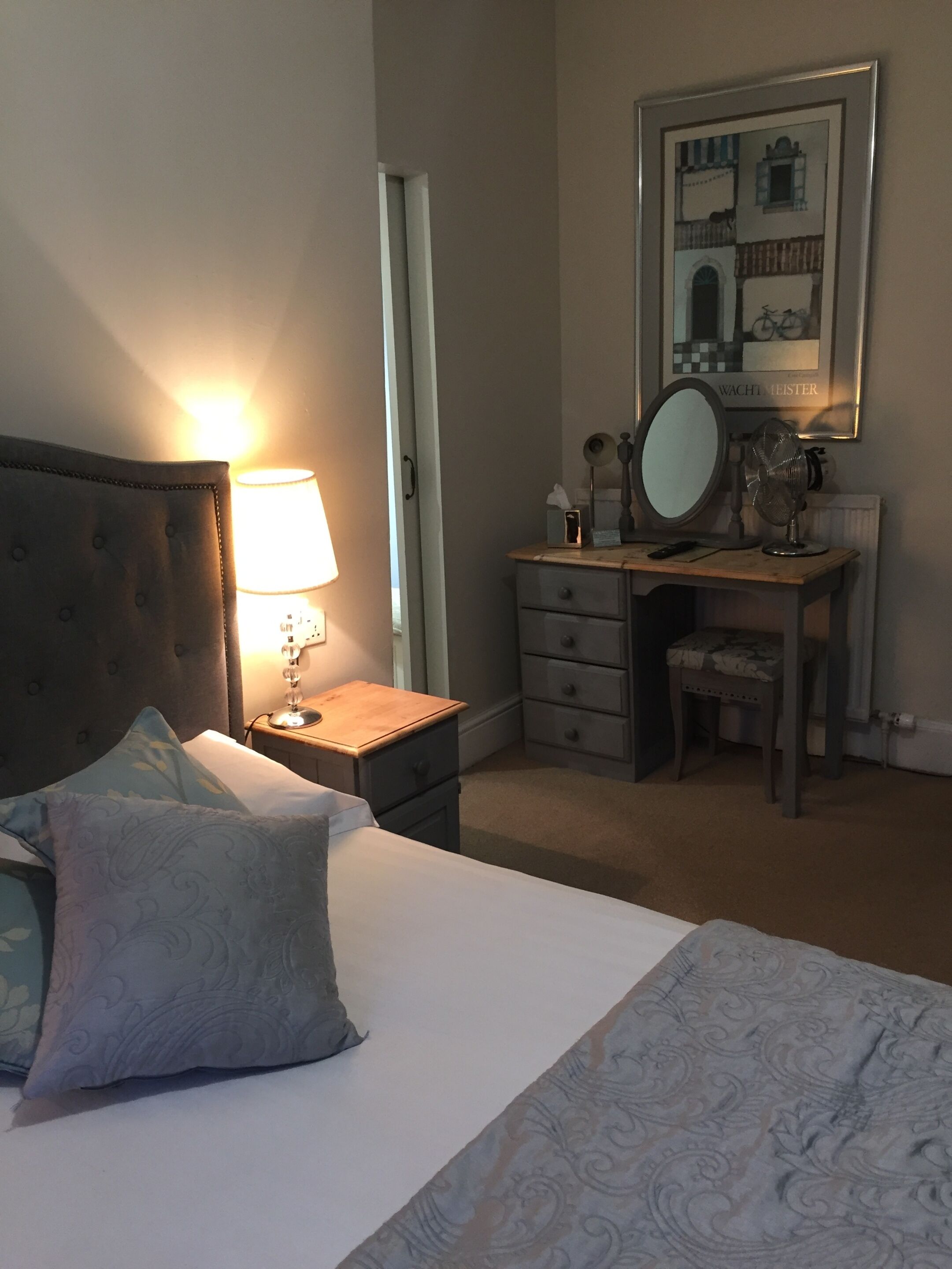 A neatly arranged bedroom with a bed, bedside lamp, dresser, and a mirror.