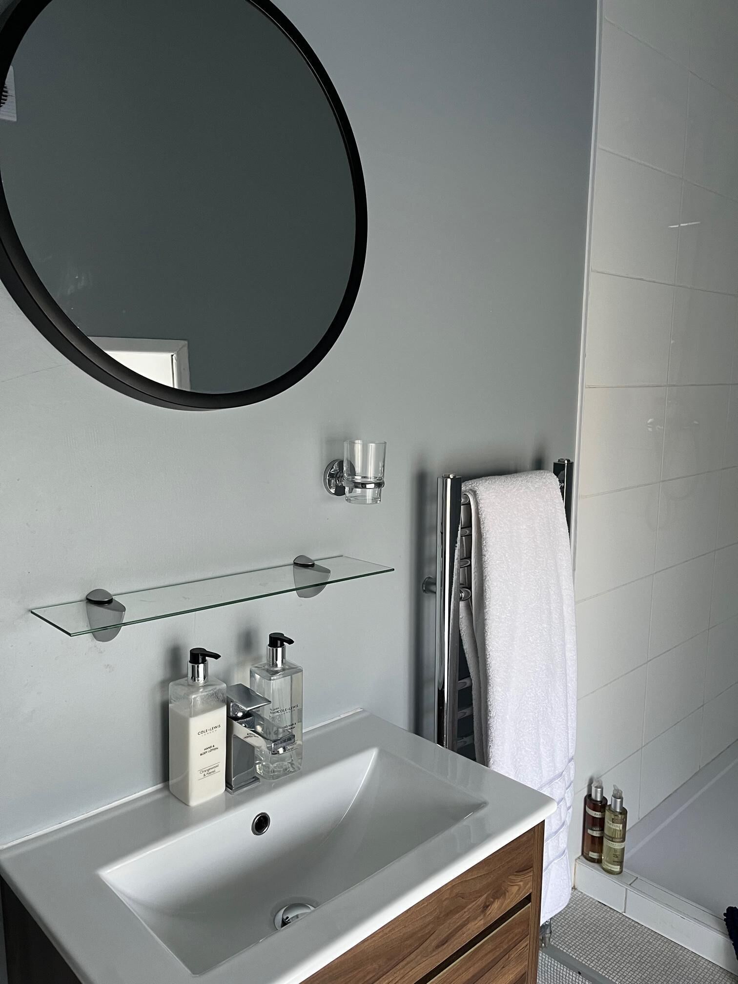 Un baño con un lavabo blanco, un espejo redondo y una repisa de cristal arriba.