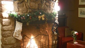 A stone fireplace with a lit fire, a Christmas garland, and a red leather sofa in a cozy room. - Castle Lodge Hotel (Ross-on-Wye)