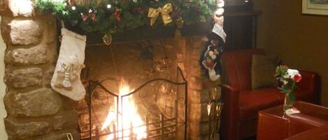 A stone fireplace with a lit fire, a Christmas garland, and a red leather sofa in a cozy room.