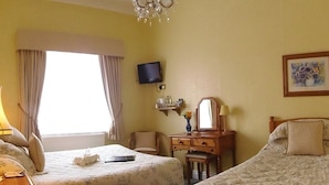 A hotel room with two beds, a television, a desk with a lamp, a chair, a dresser, and a painting on the wall. - City Guest House (York)
