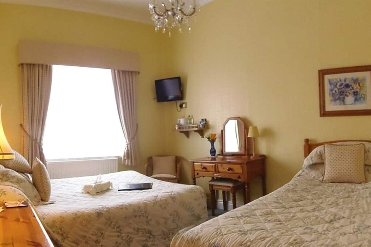 Ein Hotelzimmer mit zwei Betten, einem Fernseher, einem Schreibtisch mit Lampe, einem Sessel, einer Kommode und einem Bild an der Wand.