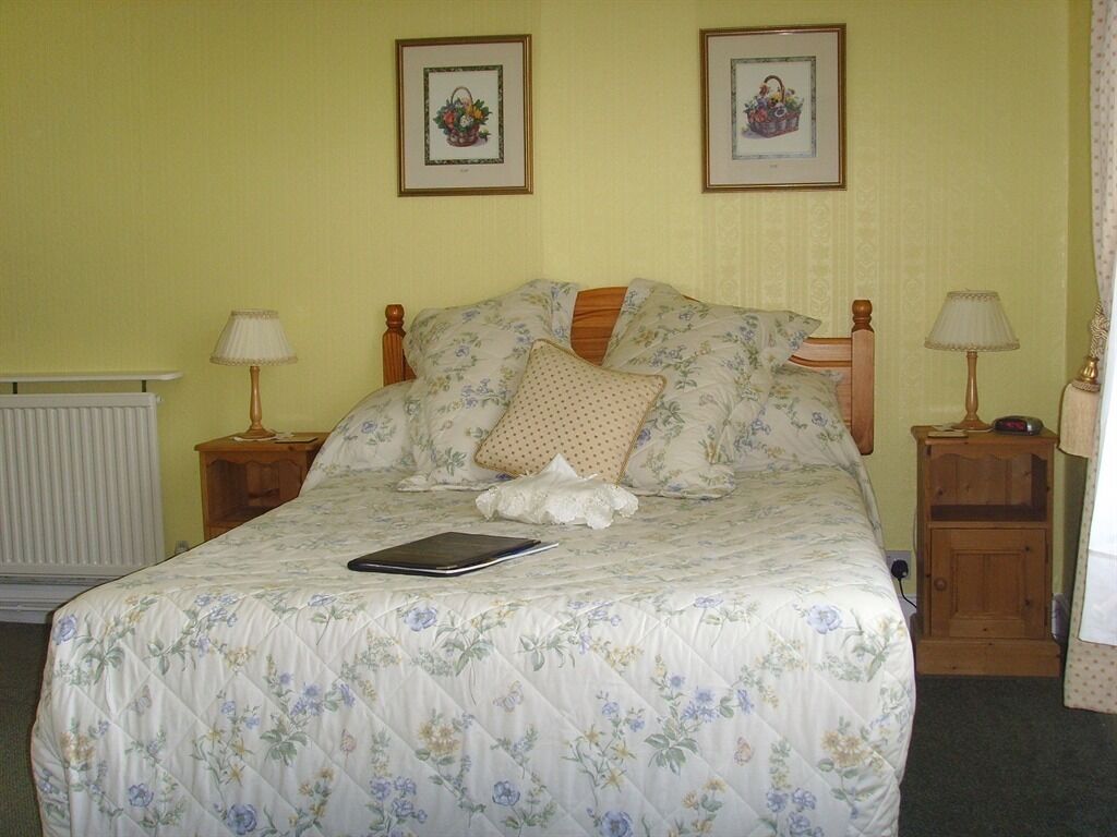 Een bed met een bloemenlaken, twee ingelijste foto's aan de muur en twee bedlampjes.