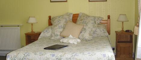 Een bed met een bloemenlaken, twee ingelijste foto's aan de muur en twee bedlampjes.
