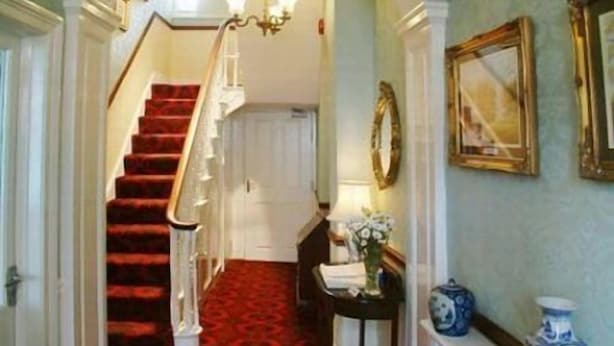 A hallway with a red carpet, a white staircase, and a chandelier. - City Guest House (York)