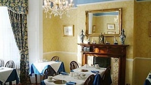 A dining area with tables set for a meal, a chandelier, and a mirror above a fireplace. - City Guest House (York)