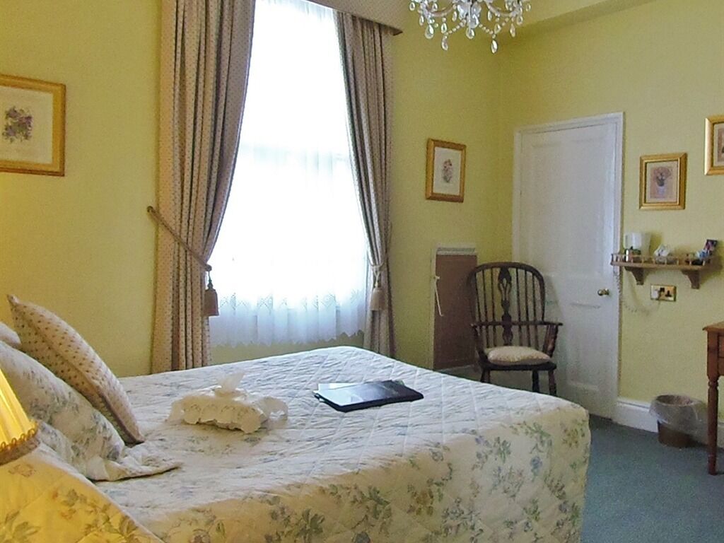 A bedroom with a bed, a chair, a door, and a chandelier.