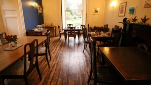 A dining area with wooden tables and chairs, a fireplace, and a view of the outdoors through a large window. - Laston House (Ilfracombe)