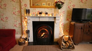 A cozy living room with a fireplace, a red sofa, a television, and a decorative mirror. - Laston House (Ilfracombe)
