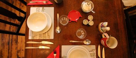 Una mesa de comedor dispuesta con platos, tazones, cubiertos y una servilleta roja.