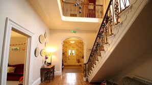 A wooden-floored hallway with a staircase on the right, leading to a door with floral wallpaper. - Laston House (Ilfracombe)