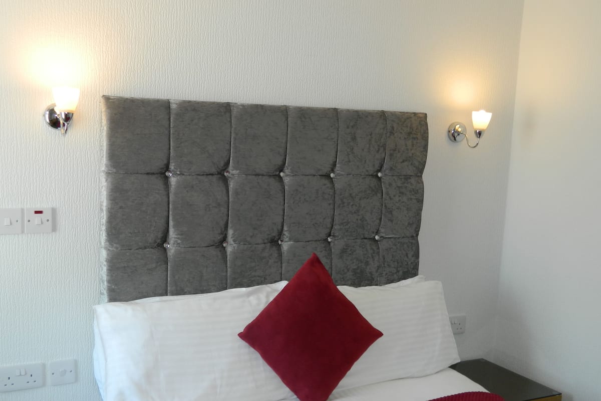 A bedroom with a tufted headboard, white bedding, a red pillow, and two bedside tables.