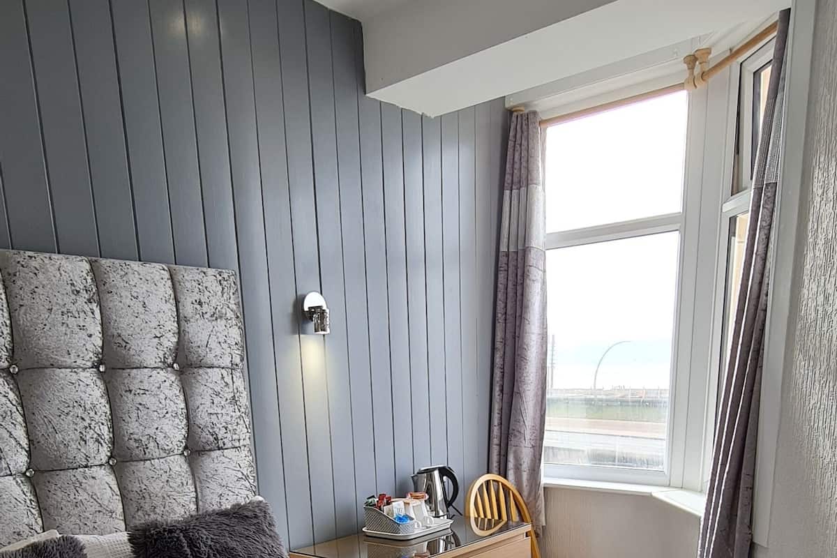 A bedroom with a bed, a nightstand, a chair, and a window with curtains.