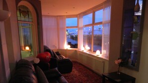 A cozy living room with a leather sofa, a red plush toy, and a vase with flowers on a small table. - Ocean Bay Hotel (Blackpool)