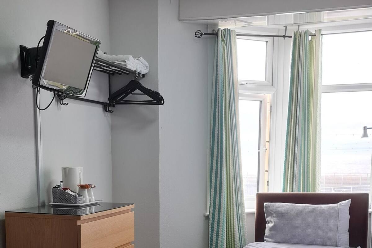 A hotel room with two beds, a desk with a computer, a mirror, and a window with curtains.